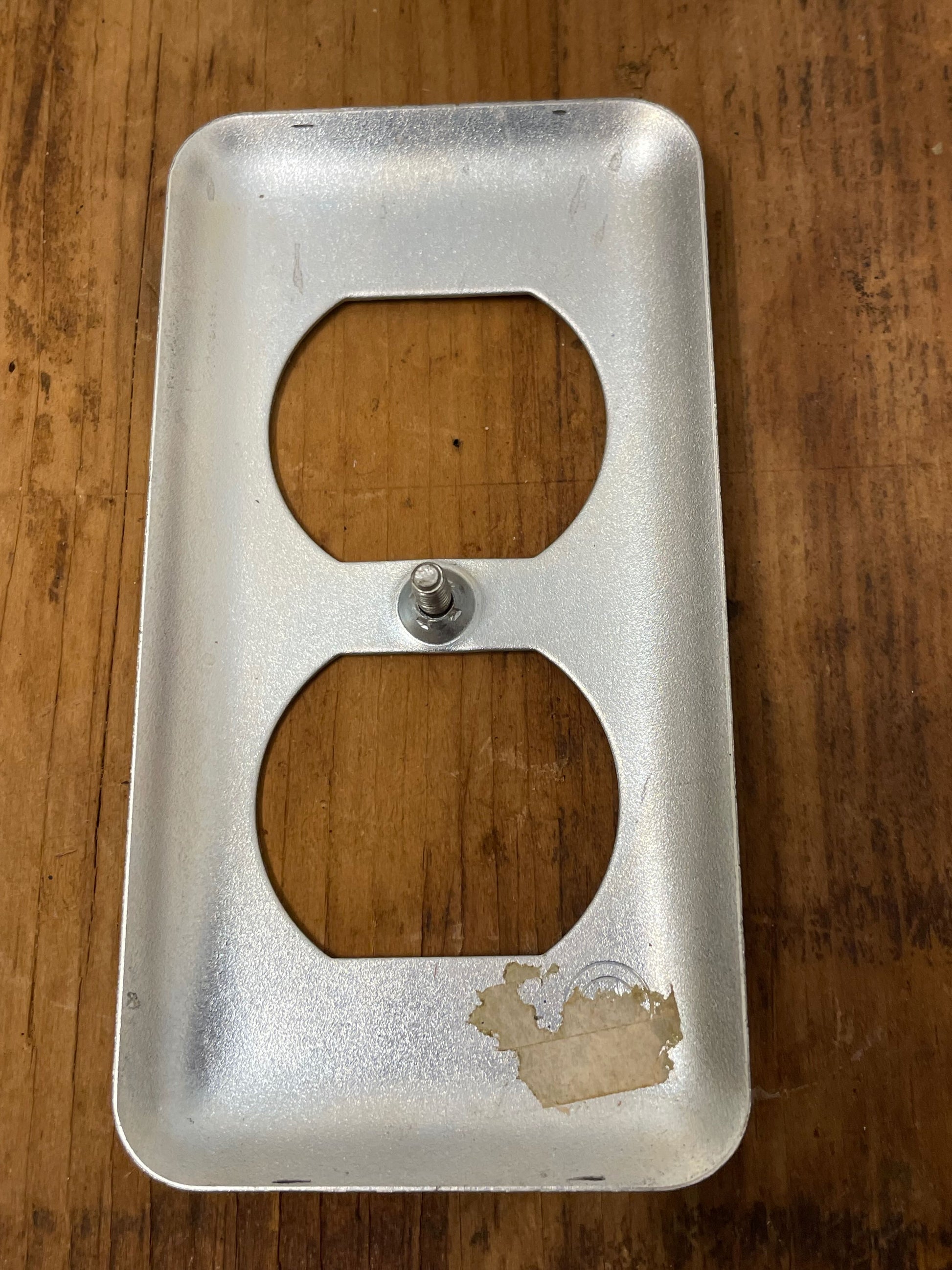 Metallic wall outlet cover with wooden inserts on a wooden surface