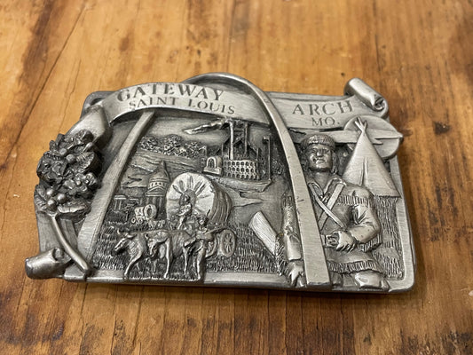 Metallic belt buckle with 'Gateway Saint Louis Arch MO' text on a wooden surface