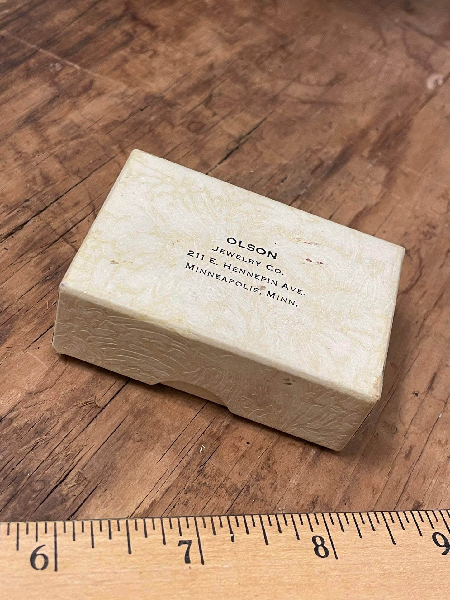 Vintage paperboard gift box with 'Olson Jewelry Co' printed on a wooden surface with a ruler for scale.