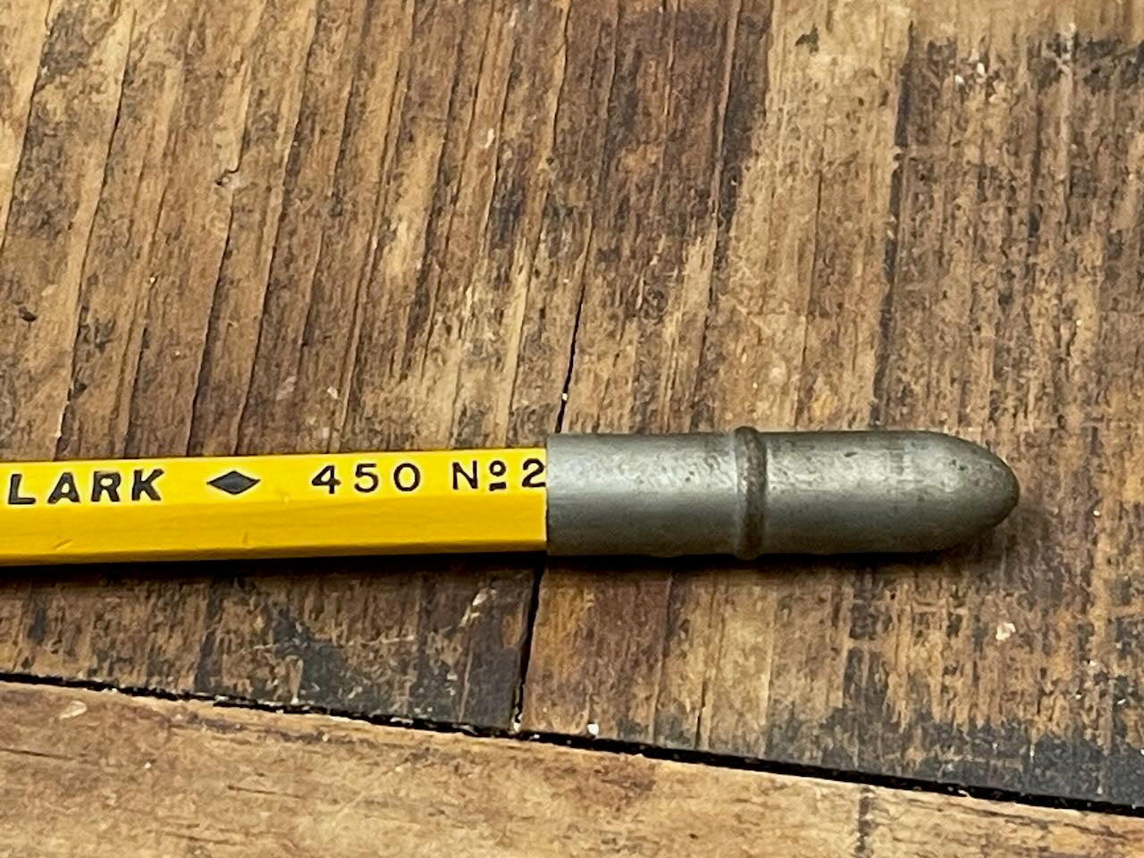 Metal pencil topper covering the eraser end of a Lark No 2 pencil, on a wooden surface