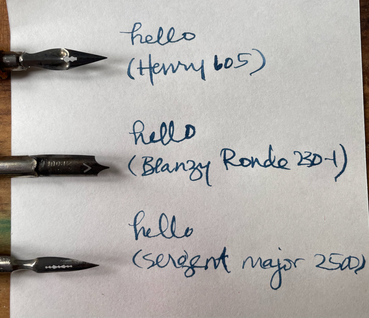 Three pen nibs displayed on a piece of paper with writing samples.