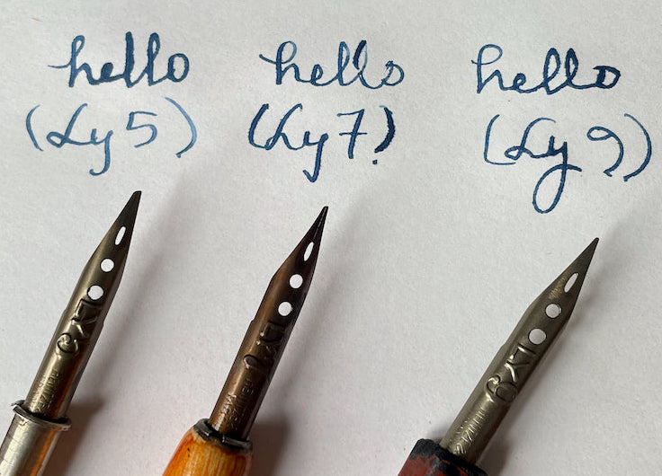 Three pen nibs on a piece of paper displaying 'hello' written three times.