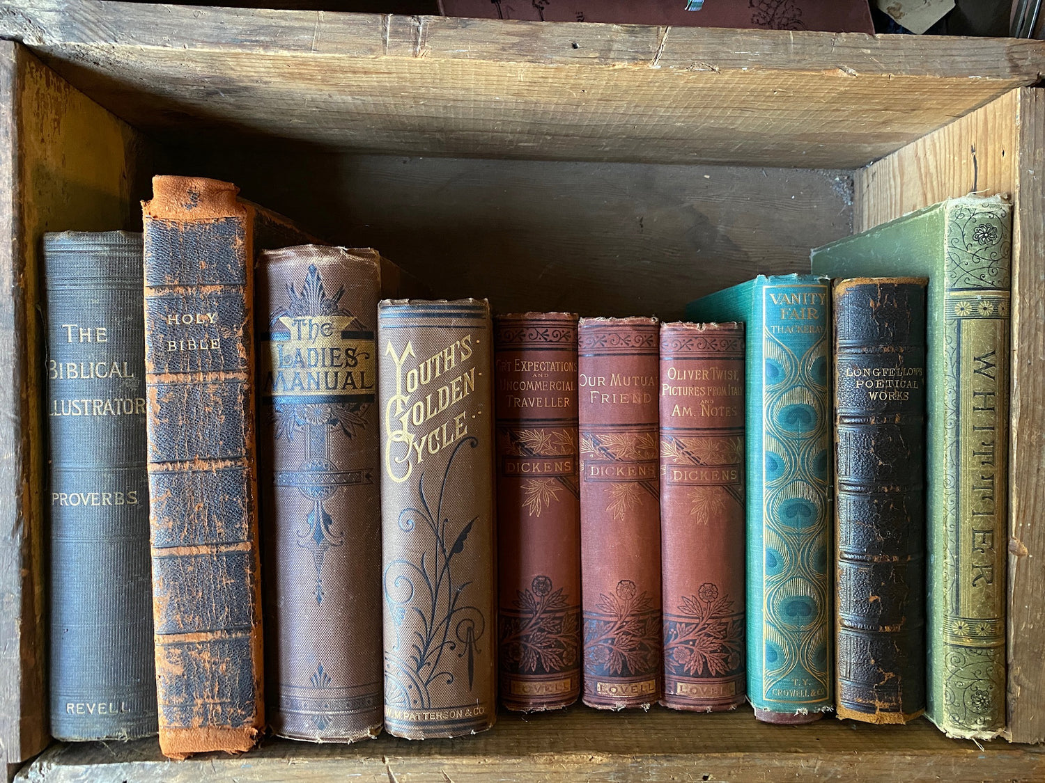 Image features ten timeworn 19th century books standing upright inside an old wooden crate.  