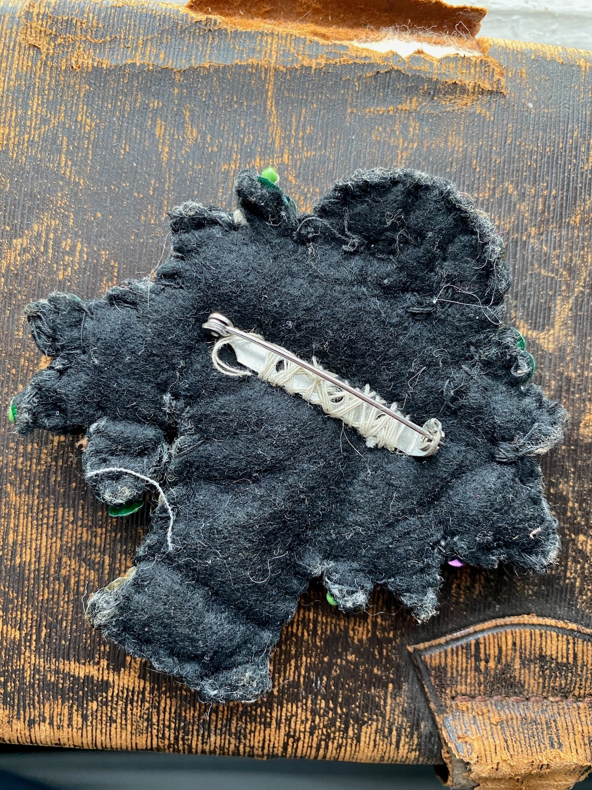 Pinback side of a handmade brooch against a distressed black surface.
