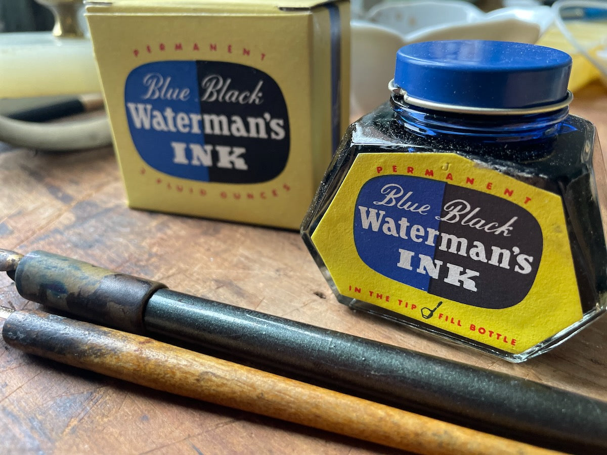 Waterman's Blue Black ink bottle with packaging and pens on a wooden surface