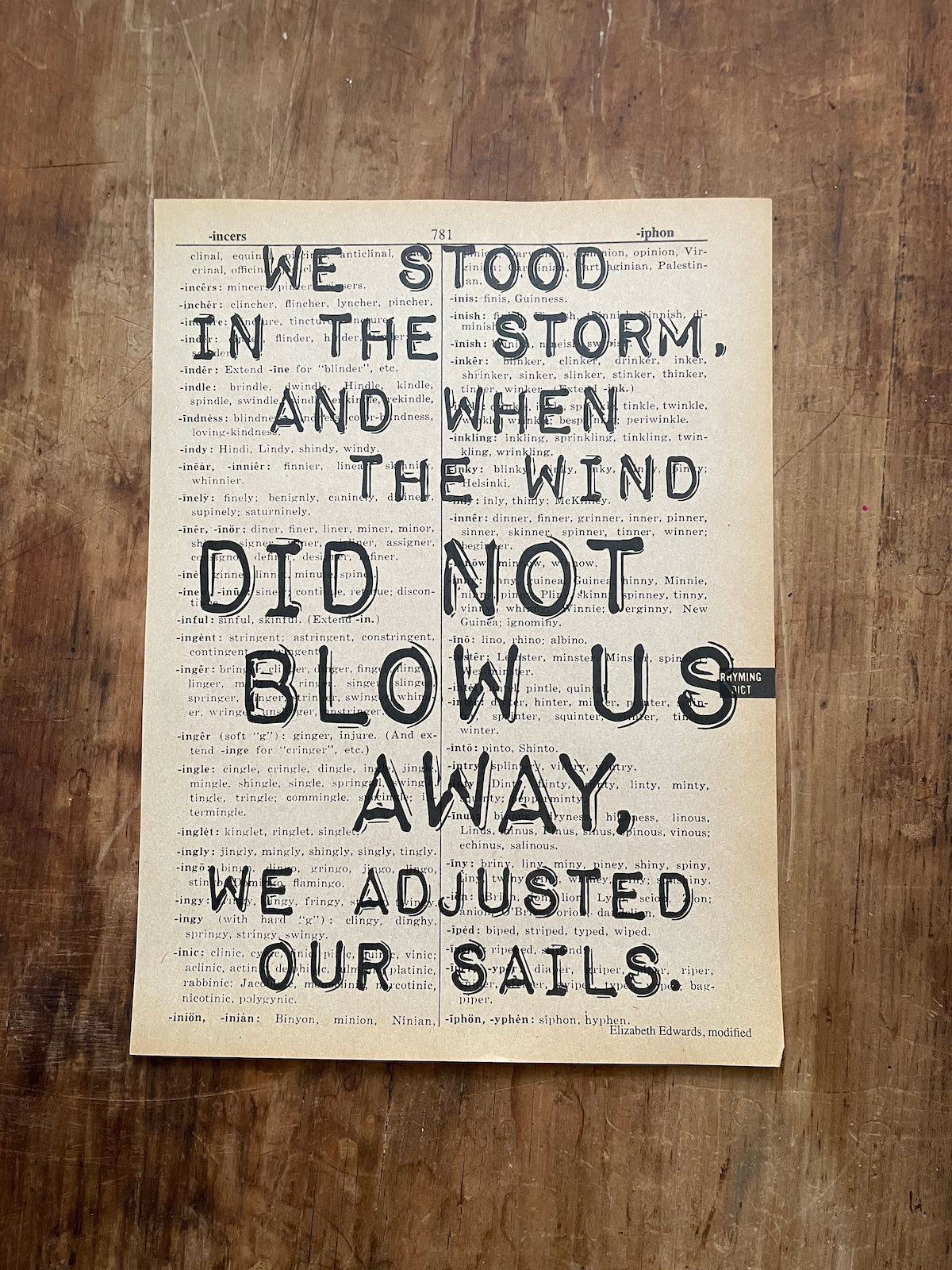 Motivational quote on a piece of paper with a wooden background: "we stood in the storm, and when the wind did not blow us away, we adjusted our sails."