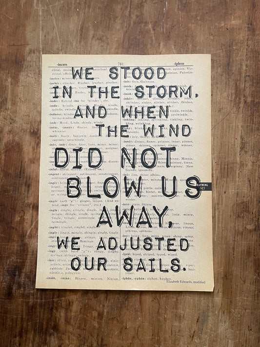 Motivational quote on a piece of paper with a wooden background: "we stood in the storm, and when the wind did not blow us away, we adjusted our sails."