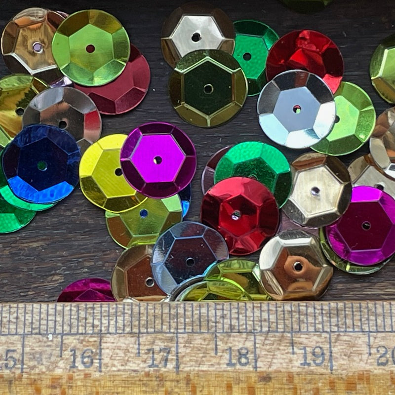 Assorted shiny multicolored sequins beside a metal ruler